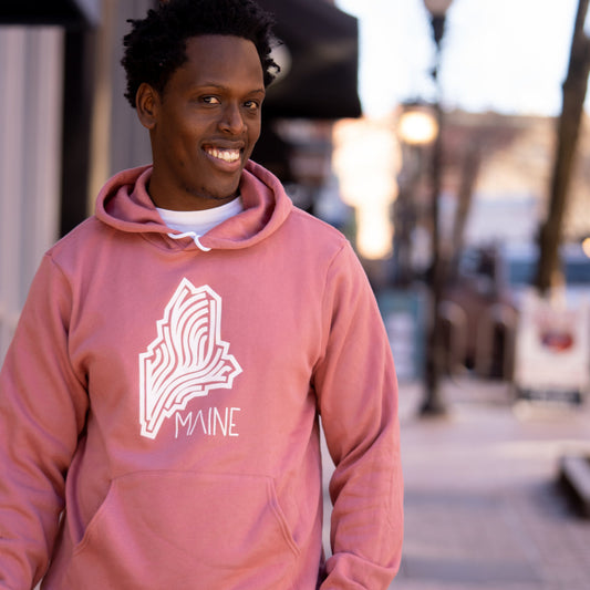 Person wearing a pink hoodie with 'Maine' design on a blurred street background