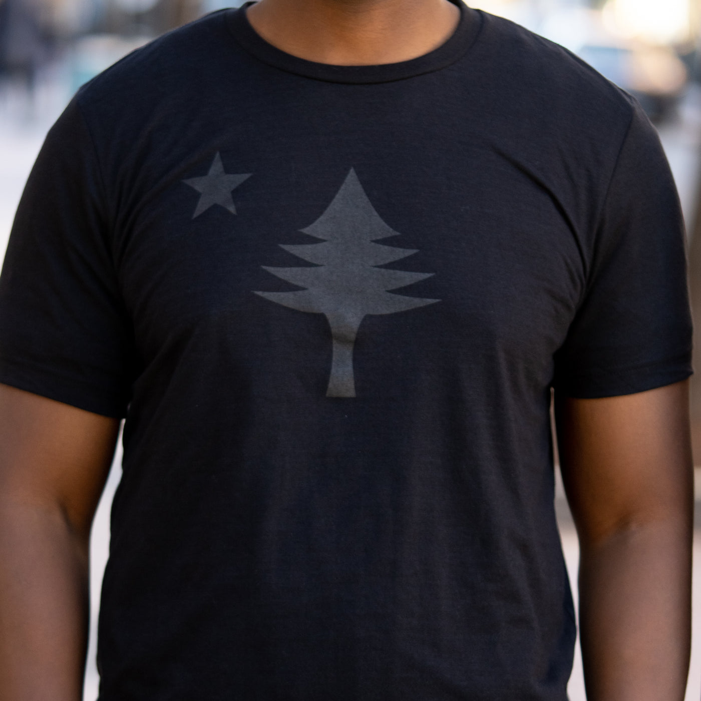 Black t-shirt with a star and tree design worn by a person.